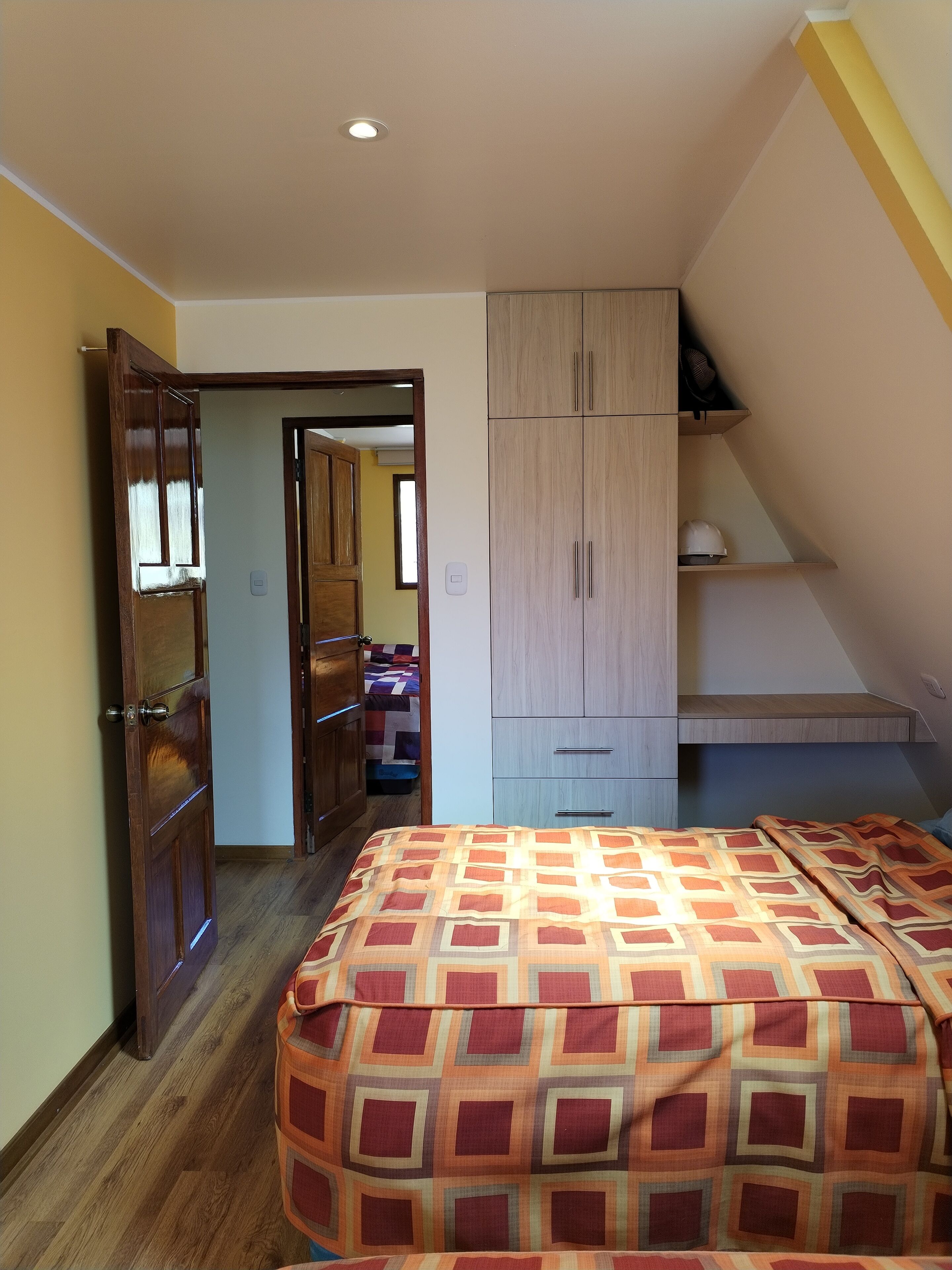 Un dormitorio con cama, armario de madera y un pequeño escritorio con silla.