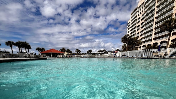 A large outdoor swimming pool with clear blue water, surrounded by a white fence and palm trees. - Premier Golf Location - Barefoot Resort! Family/dog friendly - 2 pools/beach! (North Myrtle Beach)