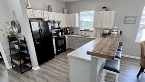 A modern kitchen with white cabinets, a black refrigerator, and a wooden island with bar stools. - Premier Golf Location - Barefoot Resort! Family/dog friendly - 2 pools/beach! (North Myrtle Beach)