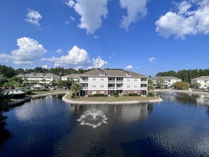 Ein mehrstöckiges Wohngebäude mit Balkonen, einem angelegten Teich und einem strahlend blauen Himmel.