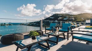 A rooftop terrace with a pool, lounge chairs, and a view of the sea and hills. - Avenue du lagon (Oyster Pond)