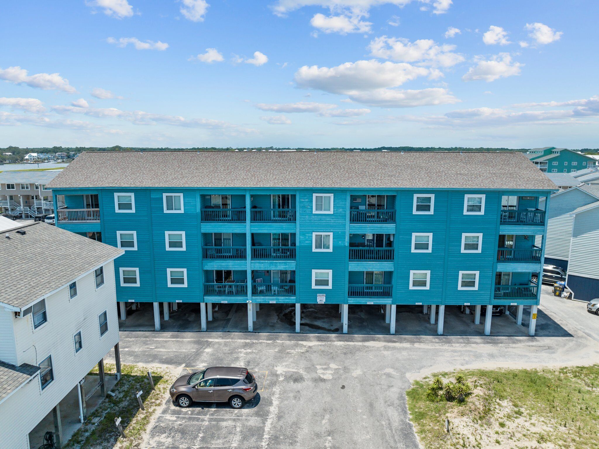 Ein mehrstöckiges Gebäude mit blauer Fassade, mehreren Balkonen und einem Parkplatz davor.