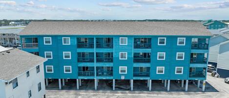 Ein mehrstöckiges Gebäude mit blauer Fassade, mehreren Balkonen und einem Parkplatz davor.