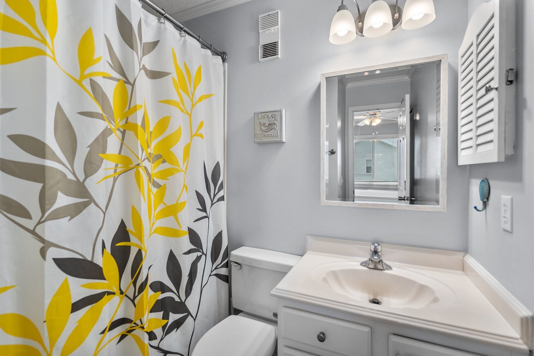 Une salle de bain équipée de toilettes, d’un lavabo et d’un rideau de douche orné d’un motif de feuilles.