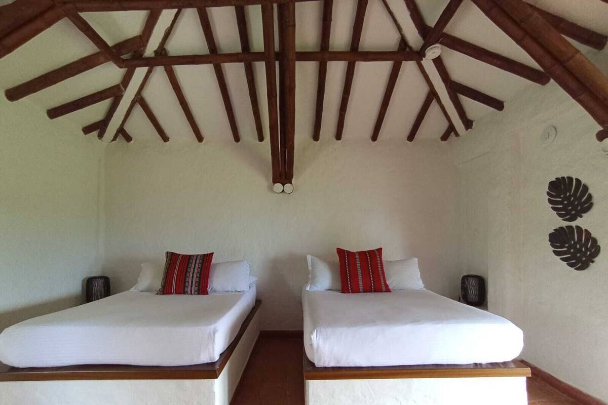 Quarto com duas camas, roupa de cama branca e estrutura de teto em madeira rústica.
