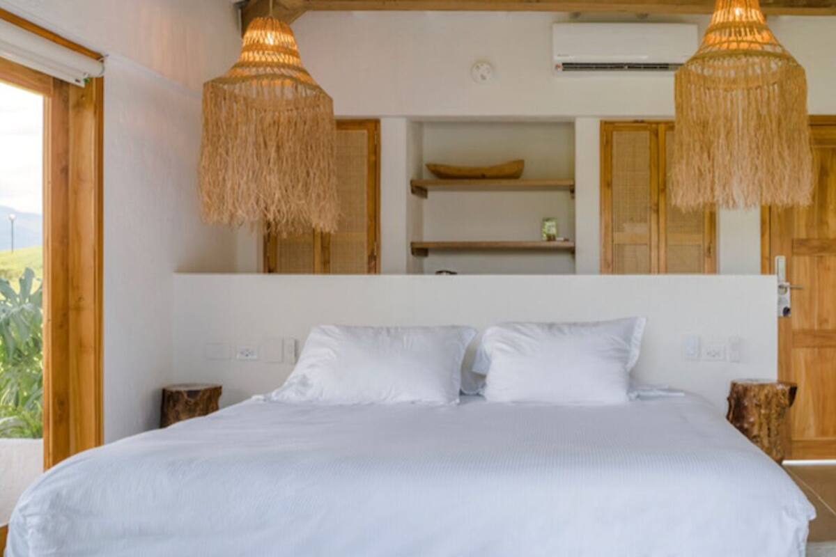 Quarto com uma cama grande, duas luminárias pendentes, estantes de madeira e uma janela com vista.