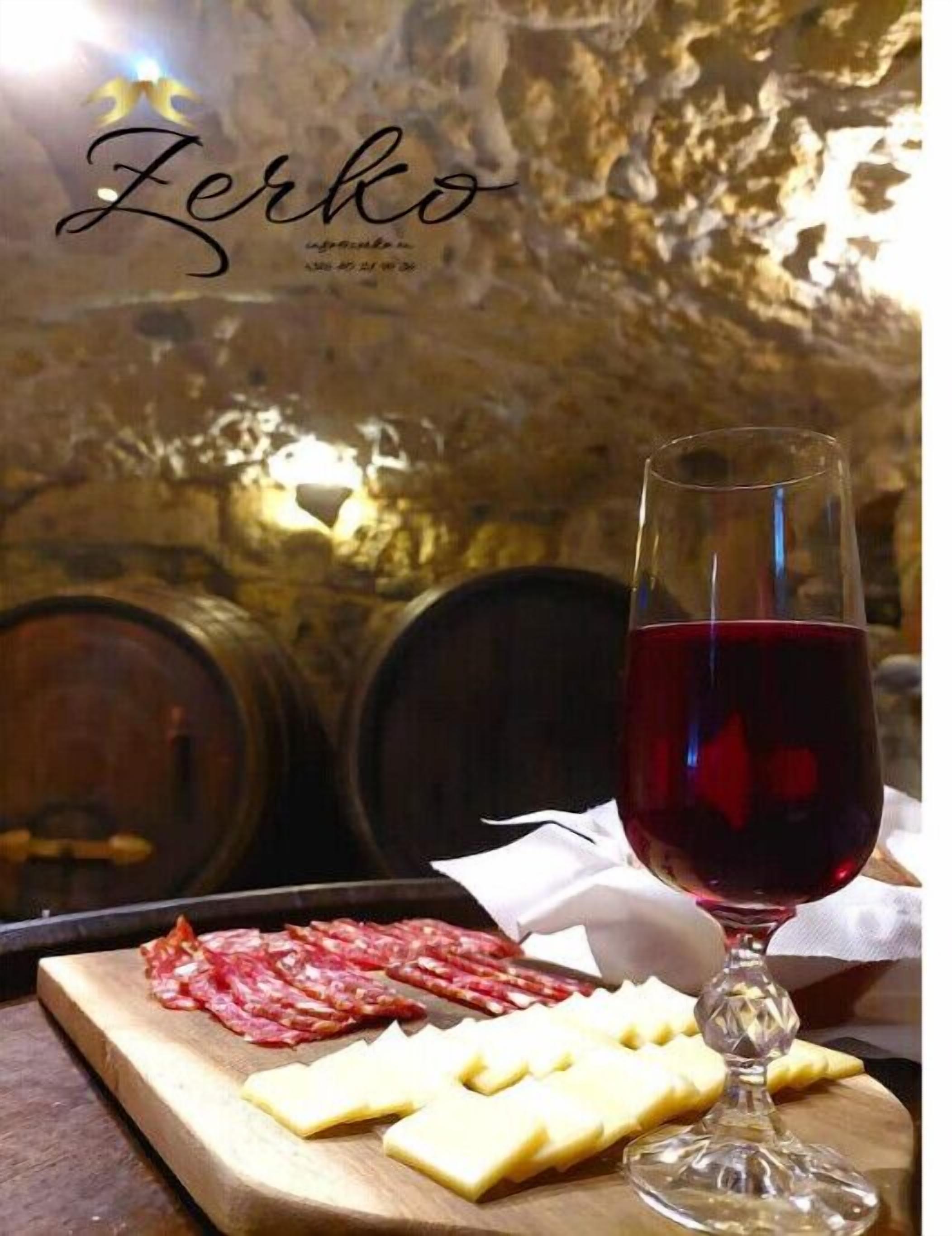 Un verre de vin rouge, une planche à découper en bois avec du fromage et de la charcuterie, et un mur en pierre en arrière-plan.