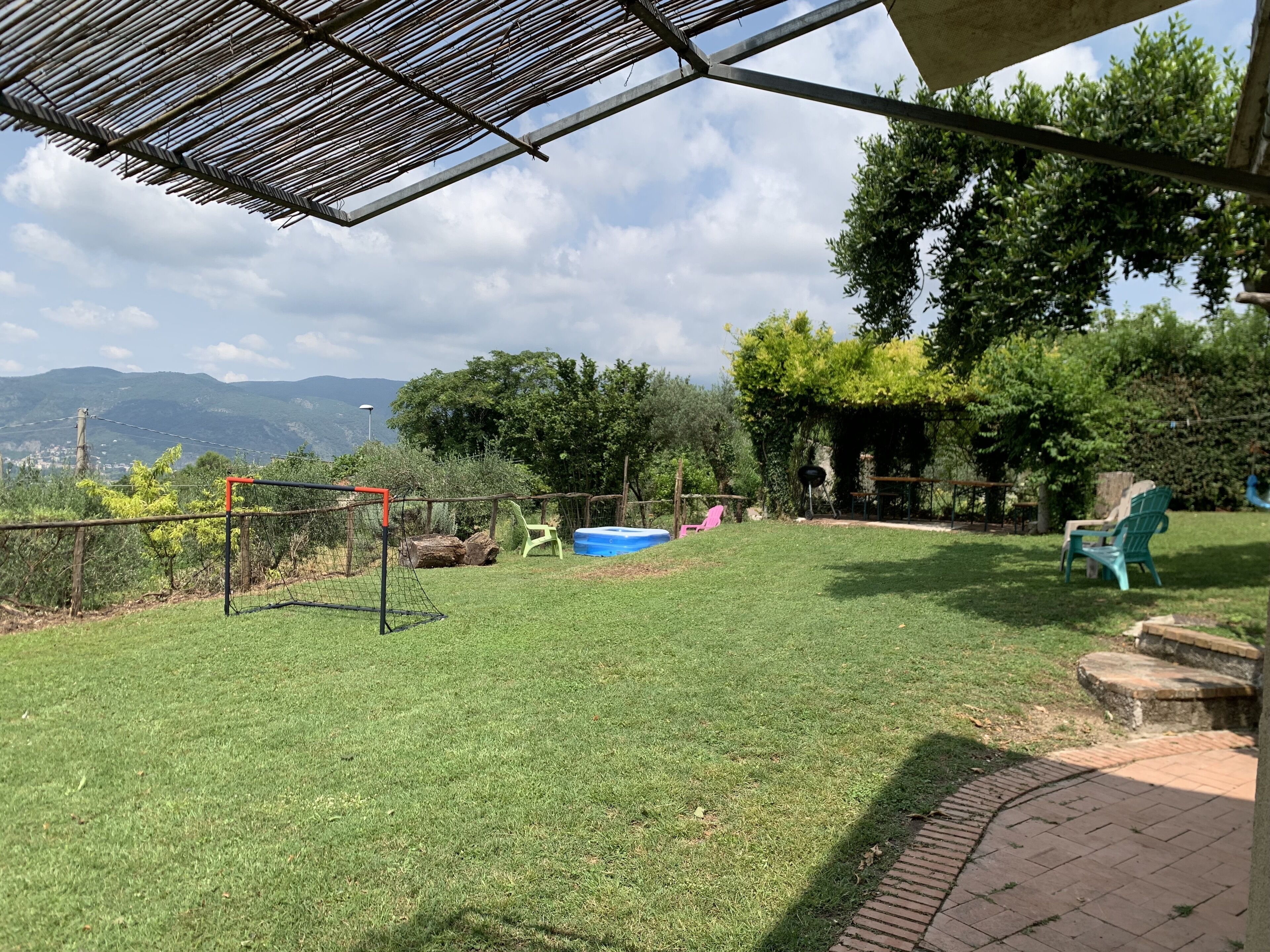 Ein grüner Garten mit Fußballtor, Teich und einer Pergola.