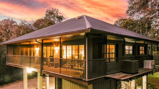 A two-story building with a balcony, large windows, and outdoor air conditioning units. - Camp Manatee - Riverfront Cabin, Stunning Views, Pet-Friendly, Hot tub + Kayaks! (Fort White)