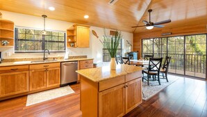 A spacious kitchen with wooden cabinets, a granite countertop, and a dining area with a large window overlooking the outdoors. - Camp Manatee - Riverfront Cabin, Stunning Views, Pet-Friendly, Hot tub + Kayaks! (Fort White)
