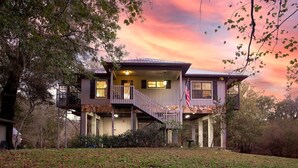 A two-story house with a balcony and a flag. - Camp Manatee - Riverfront Cabin, Stunning Views, Pet-Friendly, Hot tub + Kayaks! (Fort White)