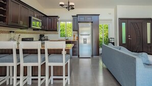 Une cuisine moderne avec des meubles en bois foncé, un réfrigérateur en acier inoxydable et un coin repas avec des chaises blanches et une table.