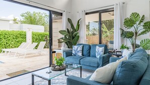 Un salon moderne avec un canapé bleu, une table basse en verre et de grandes fenêtres donnant sur un jardin.