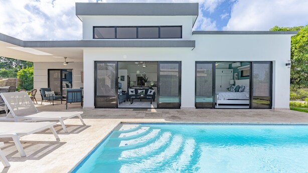 Une maison moderne dotée d’une piscine, de grandes portes vitrées et d’un espace patio.