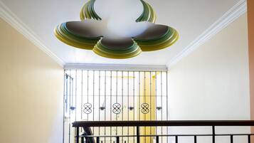 Una escalera con barandilla negra, techo blanco y un portal de metal en la ventana.