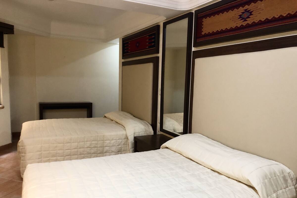 Habitación de hotel con dos camas, un espejo grande y una mesita pequeña.