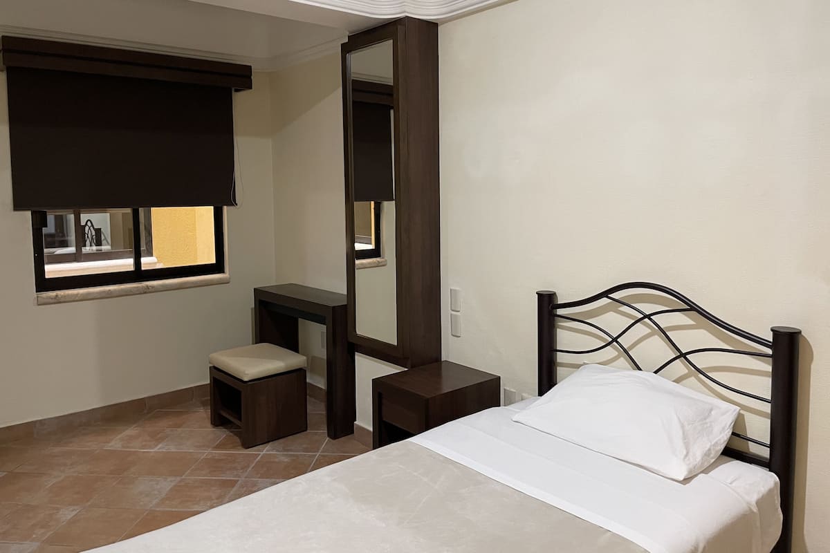 Un dormitorio con cama, mesita de noche, espejo y ventana con persianas.