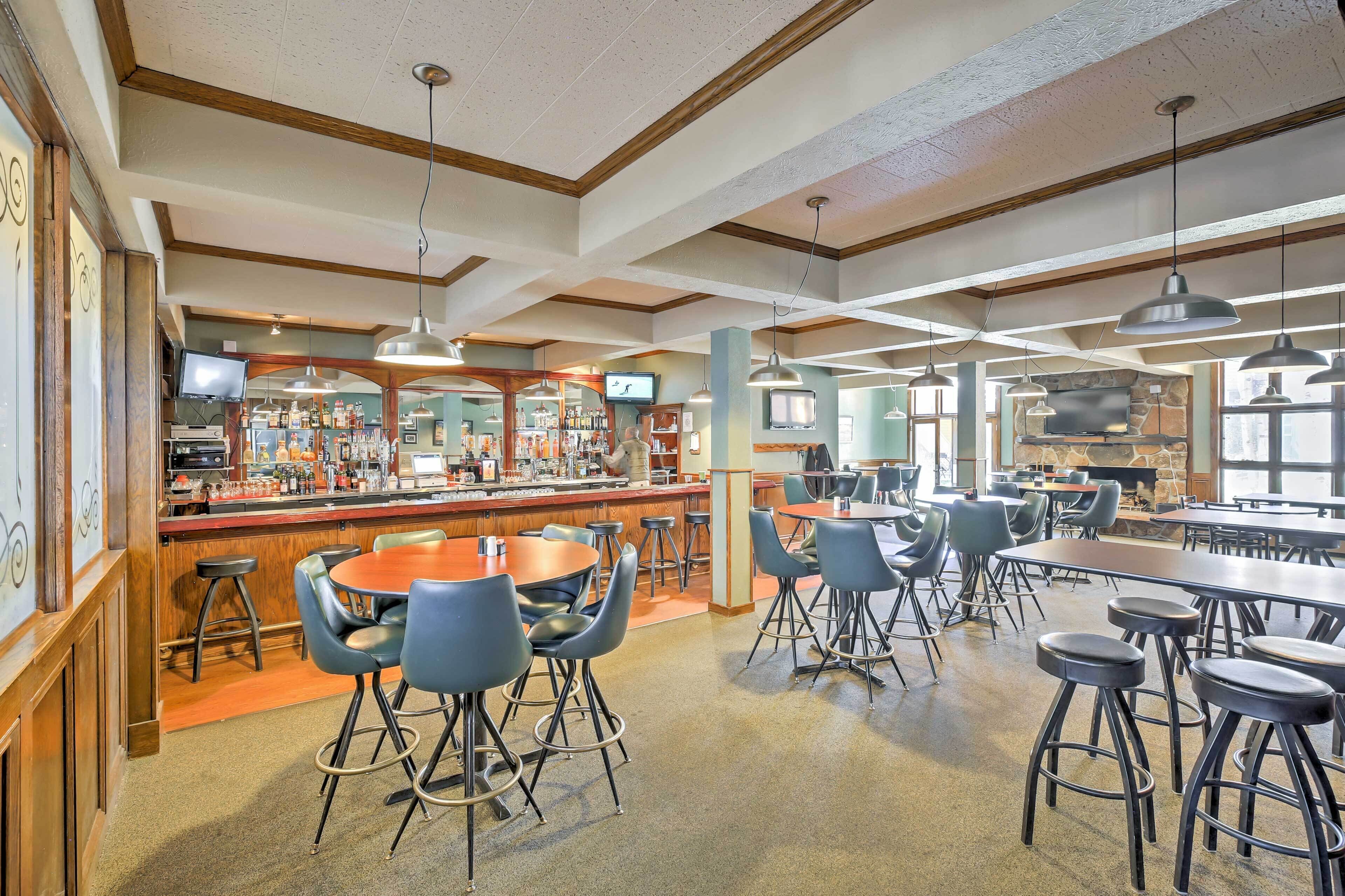 A spacious bar area with multiple seating options, a counter with a television, and a stone fireplace.