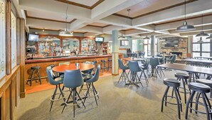 A spacious bar area with multiple seating options, a counter with a television, and a stone fireplace.