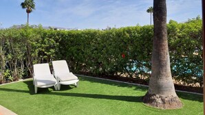 A patio with two white lounge chairs and a palm tree.