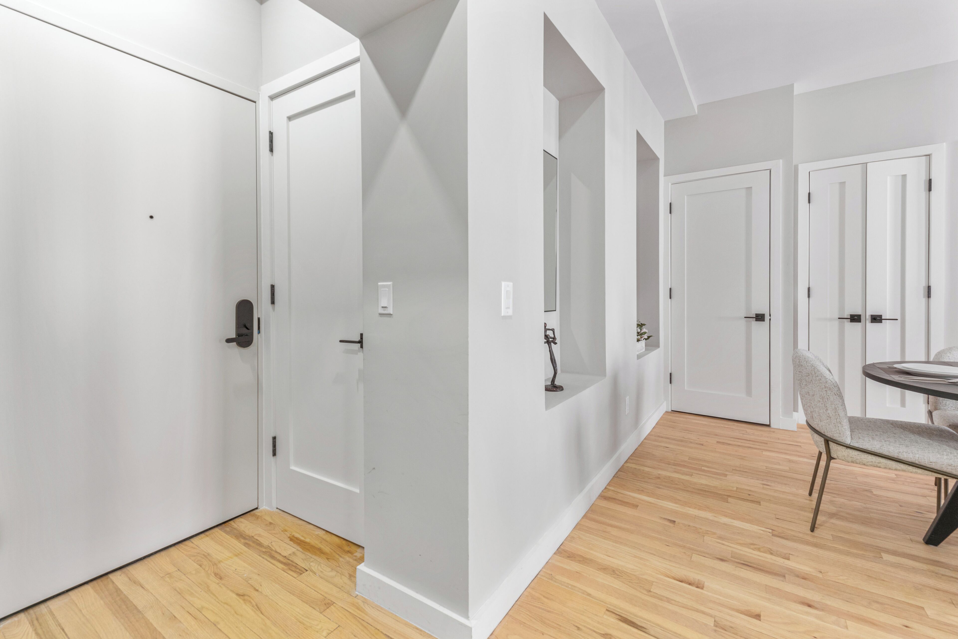 Un pasillo con puertas blancas, una zona de comedor con mesa y sillas, y suelo de madera.