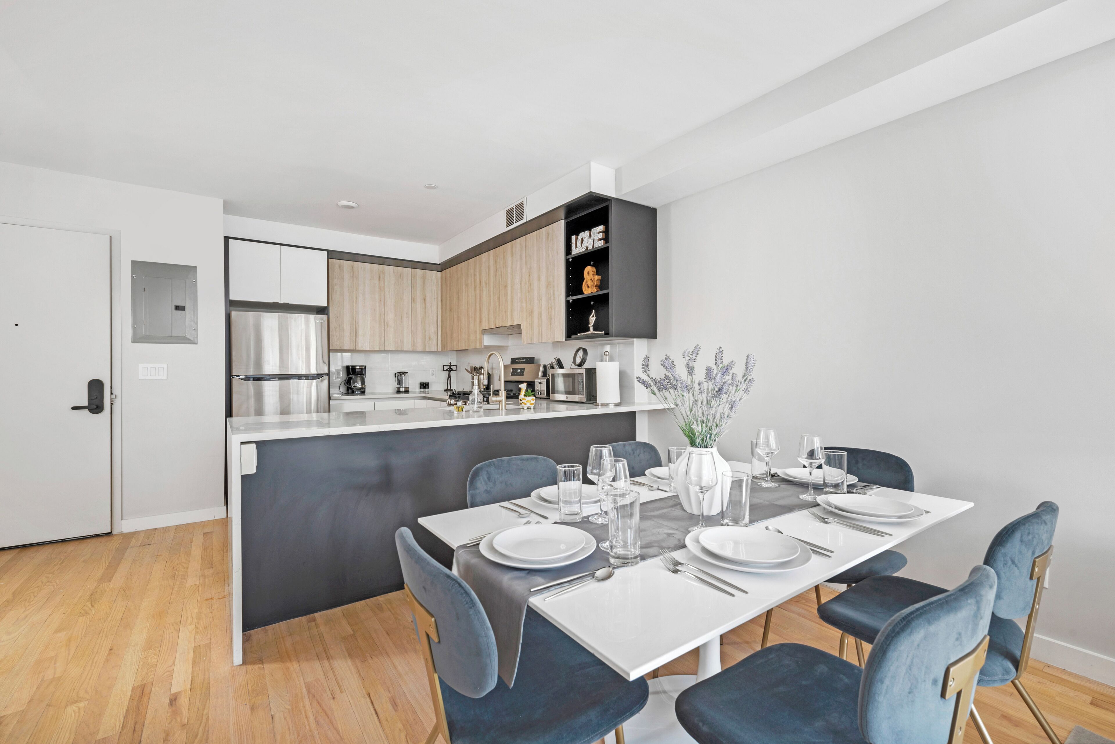 A modern kitchen with a central island, wooden cabinets, and a black shelf with the word "LOVE" on it.