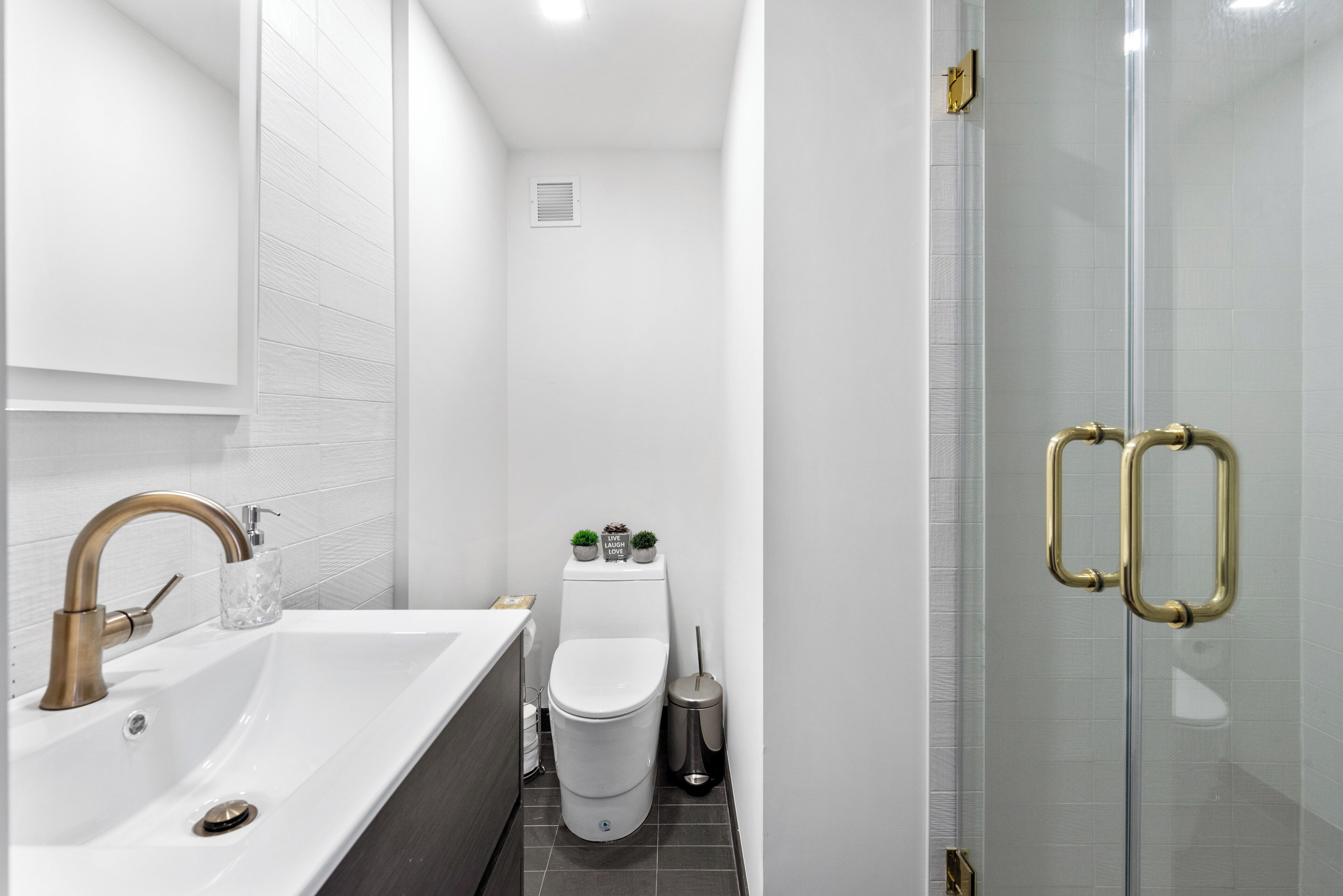 Ein modernes Badezimmer mit einem weißen Waschbecken, einem goldenen Wasserhahn und einer Duschkabine aus Glas.
