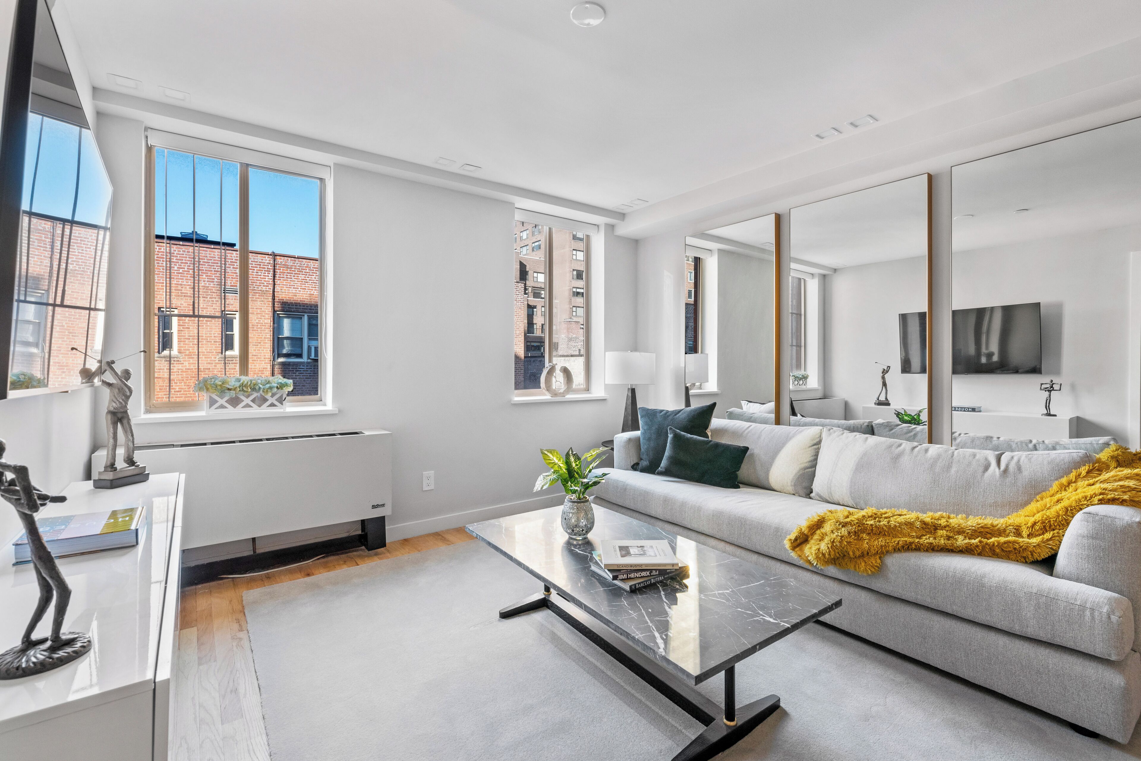 A modern living room with a grey sofa, a coffee table, and a large window offering a view of a brick building.