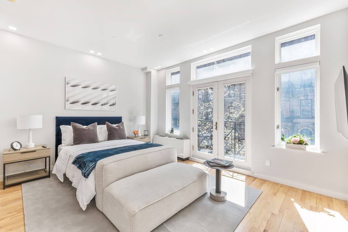 A modern bedroom with a large bed, a bedside table, a nightstand, and a view of the city through large windows.