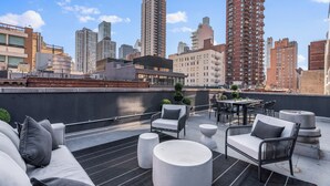 A rooftop terrace with outdoor seating, a city skyline view, and a modern building facade. - The Sixty Two (New York)
