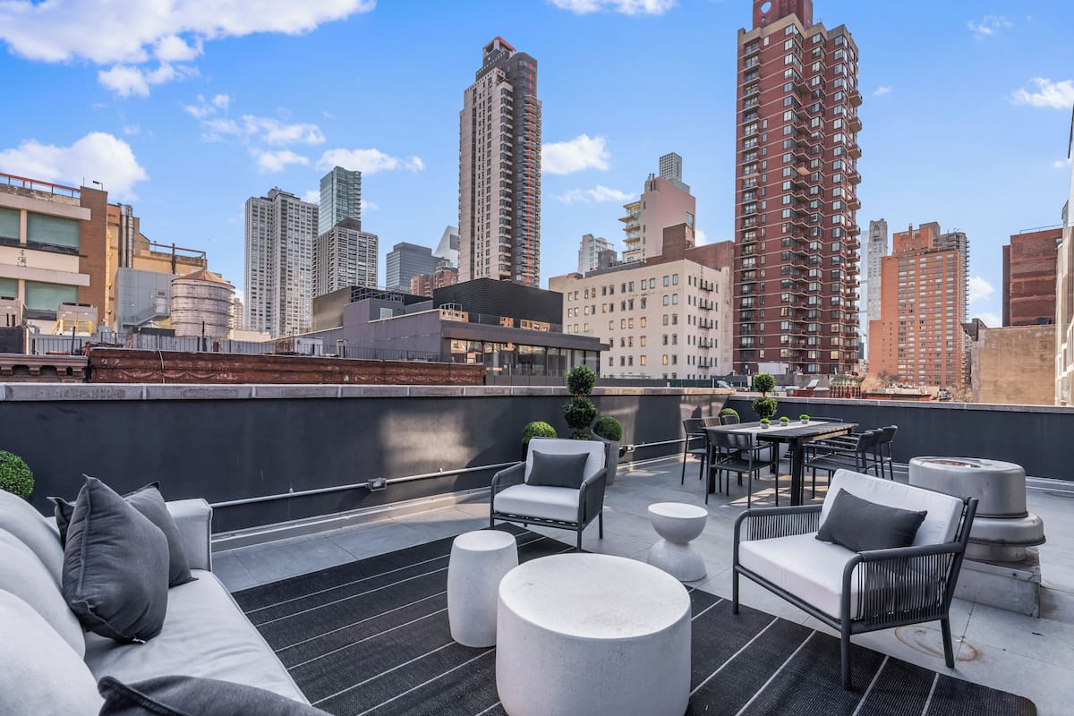 A rooftop terrace with outdoor seating, a city skyline view, and a modern building facade.