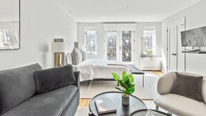 A modern living room with a grey sofa, a coffee table with a plant, and a bed with a white duvet. - The Sixty Two (New York)