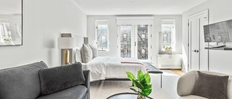 Una sala de estar moderna con un sofá gris, una mesa de centro con una planta y una cama con edredón blanco.