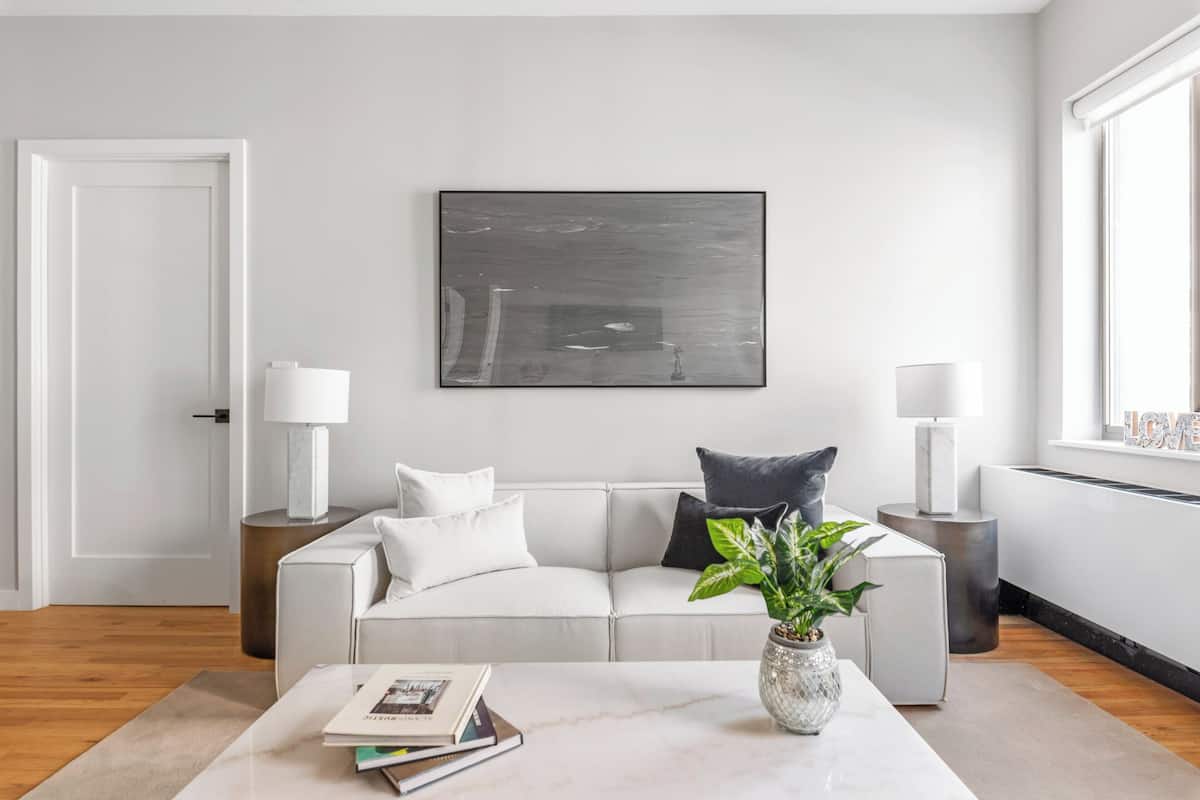 A modern living room with a white sofa, a coffee table with books and a plant, and a large abstract painting on the wall.