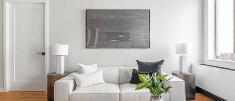 Una sala de estar moderna con un sofá blanco, una mesa de centro con libros y una planta, y un cuadro abstracto grande en la pared.