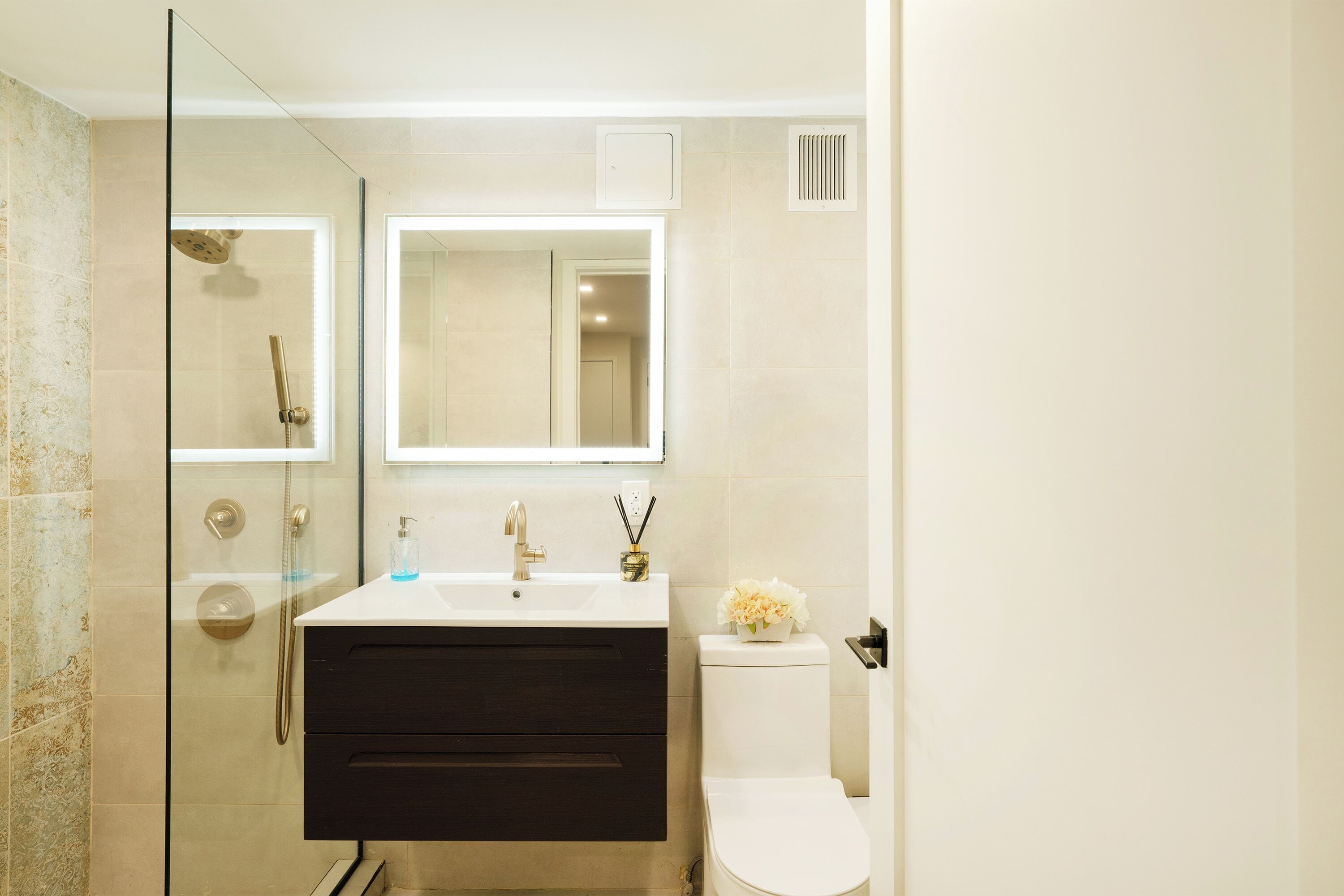 A modern bathroom with a glass-enclosed shower, a white sink with a gold faucet, and a white toilet.
