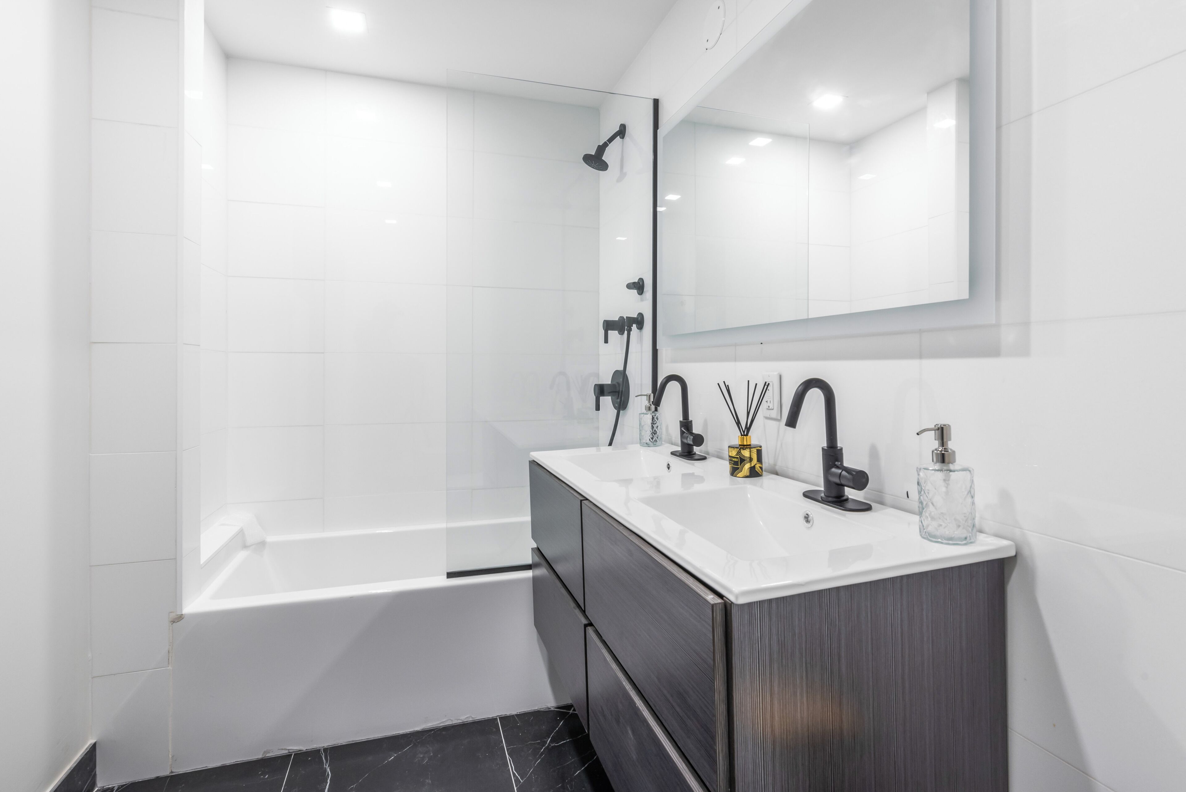 A modern bathroom with a white vanity, black marble floor, and a large mirror above the sink.