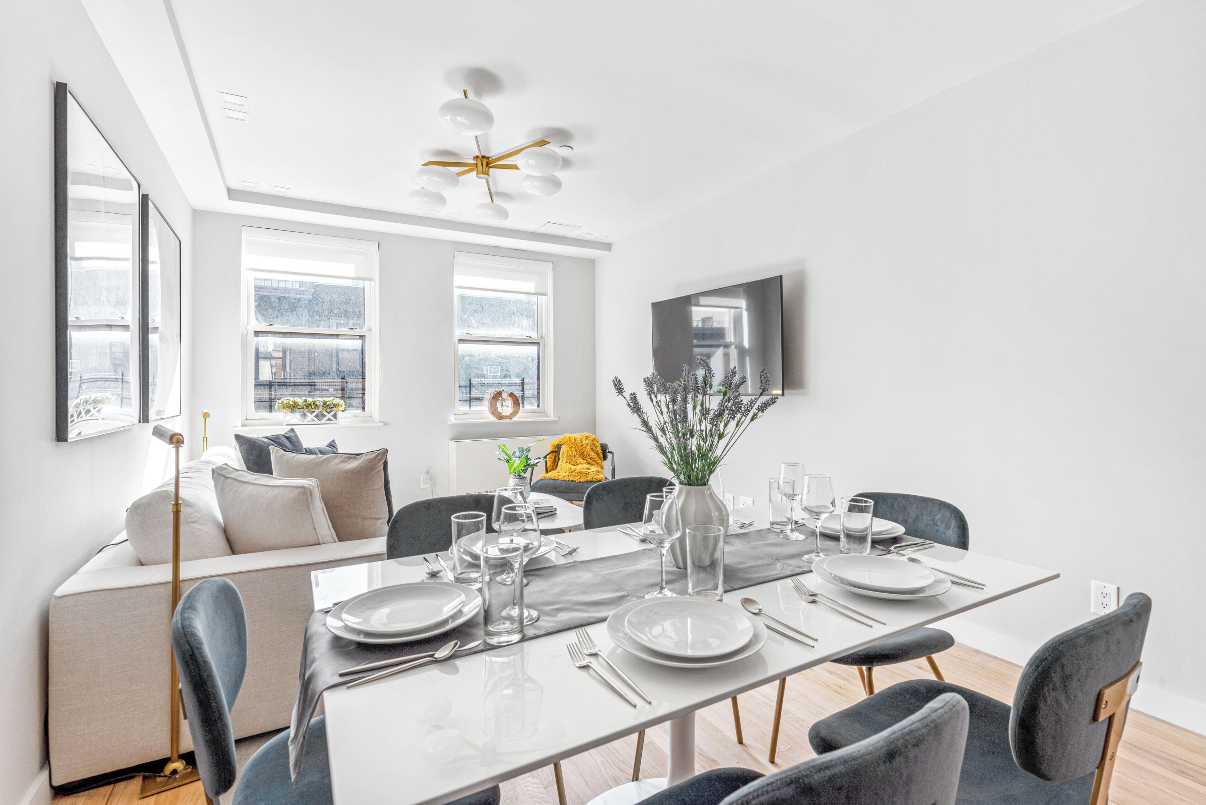 Een moderne eethoek met een witte tafel voor vier personen, grijze stoelen en een groot raam met uitzicht.