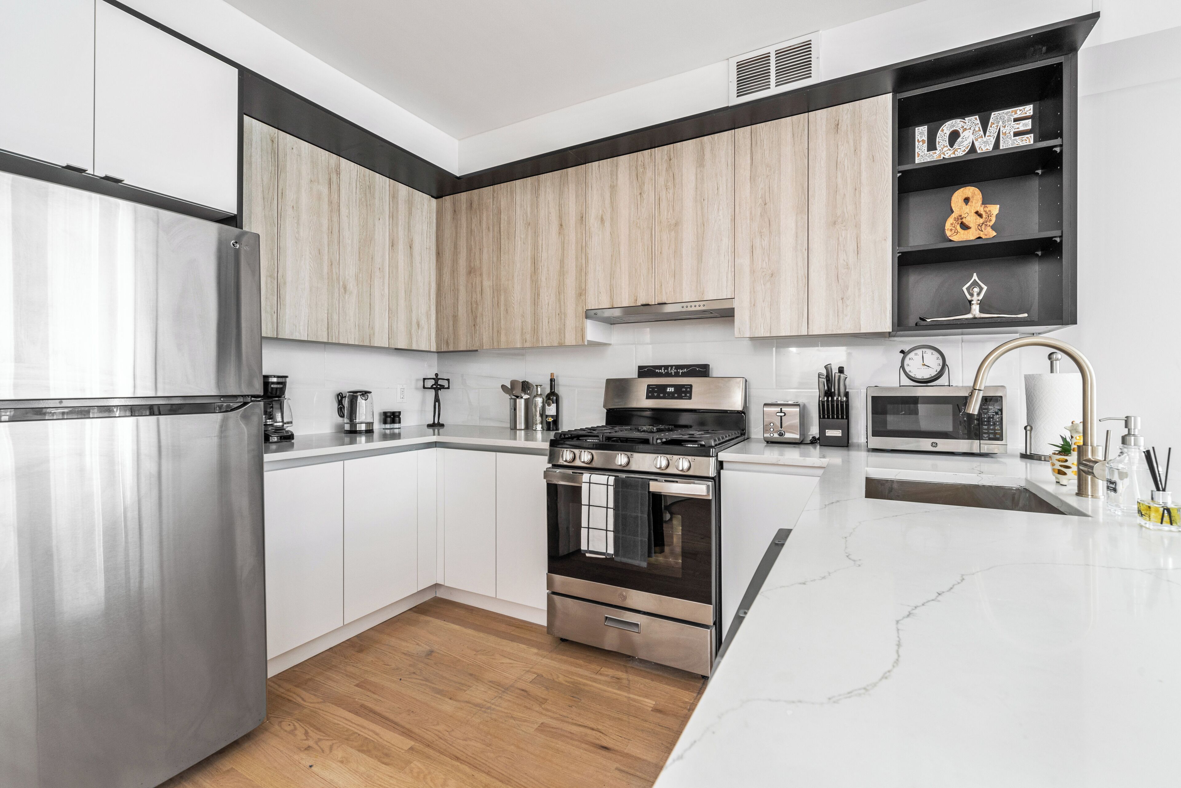 A modern kitchen with stainless steel appliances, white cabinetry, and a marble countertop.