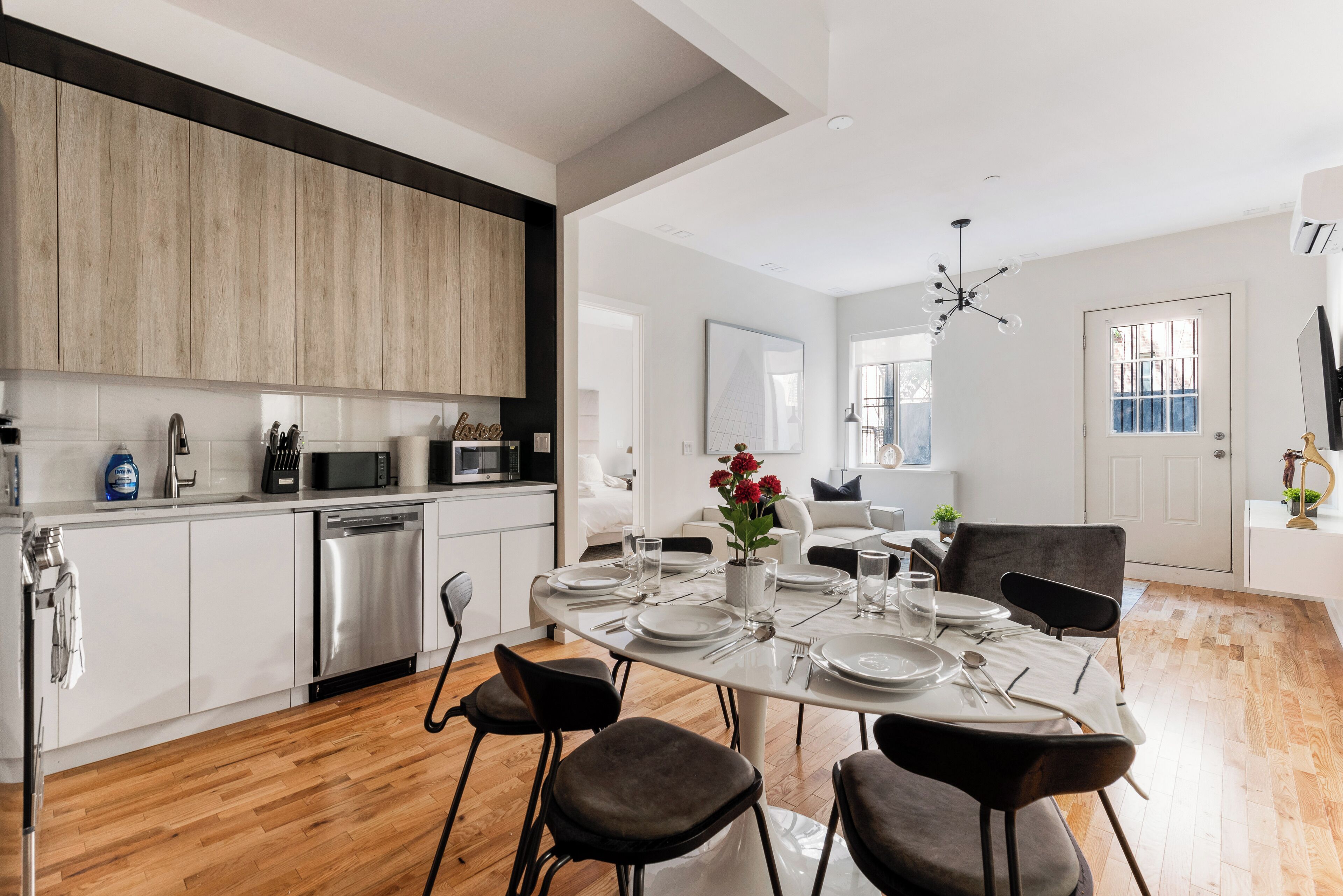 A modern kitchen with white cabinets, a dishwasher, and a dining area with a round table set for four.