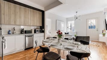 A modern kitchen with white cabinets, a dishwasher, and a dining area with a round table set for four.