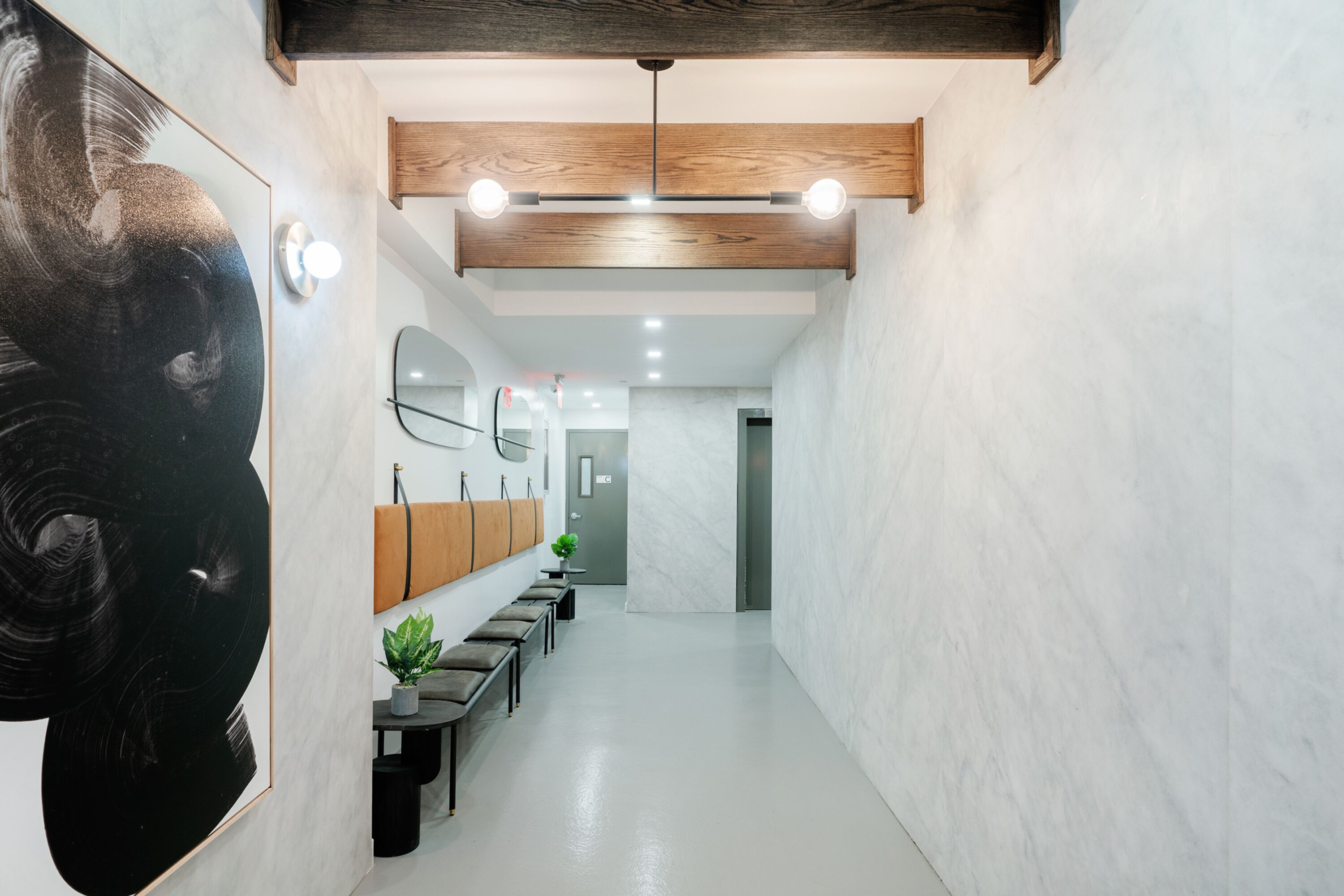 A modern hallway with a wooden ceiling, a black abstract painting, a row of benches, and a wall-mounted mirror.