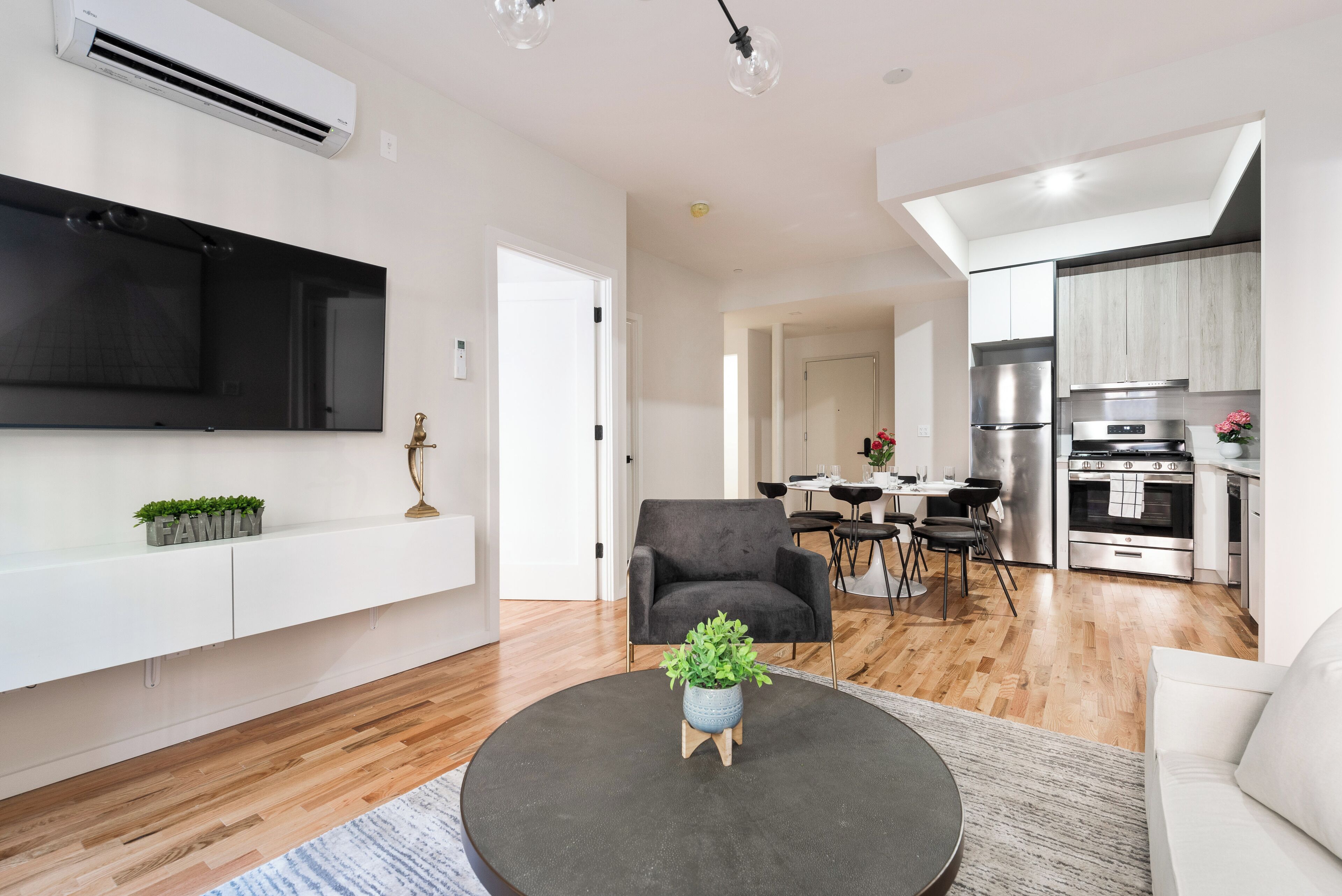 A modern living room with a flat-screen TV, a round coffee table with a plant, and a grey sofa.