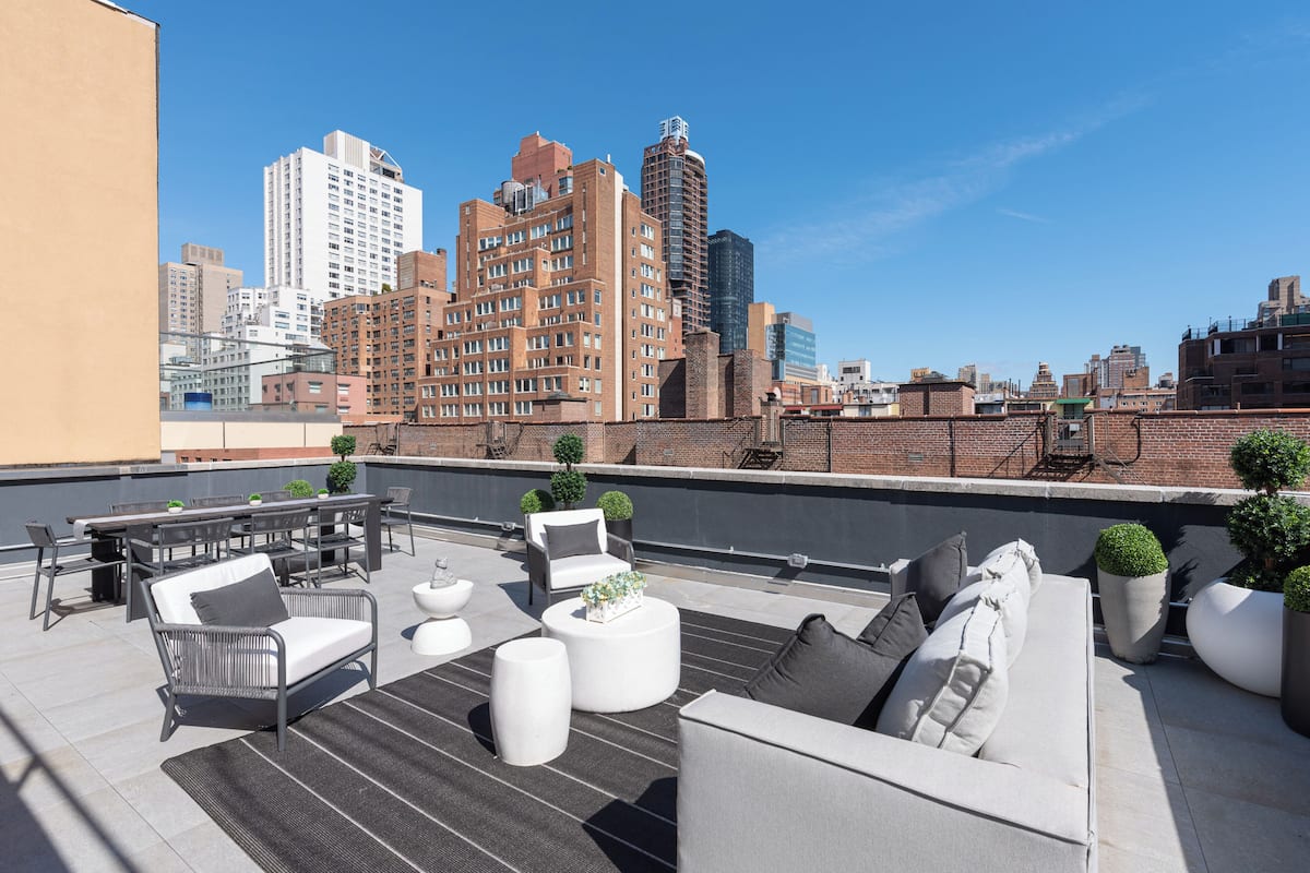 A rooftop terrace with outdoor seating, including sofas and tables, and a city skyline in the background.