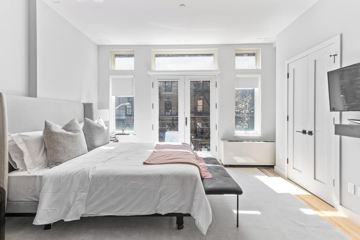 A modern bedroom with a large bed, a bench, and a TV on the right.