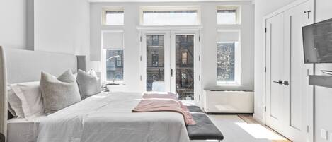 A modern bedroom with a large bed, a bench, and a TV on the right.