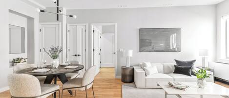 A modern living room with a dining area, white furniture, and a large abstract painting on the wall.
