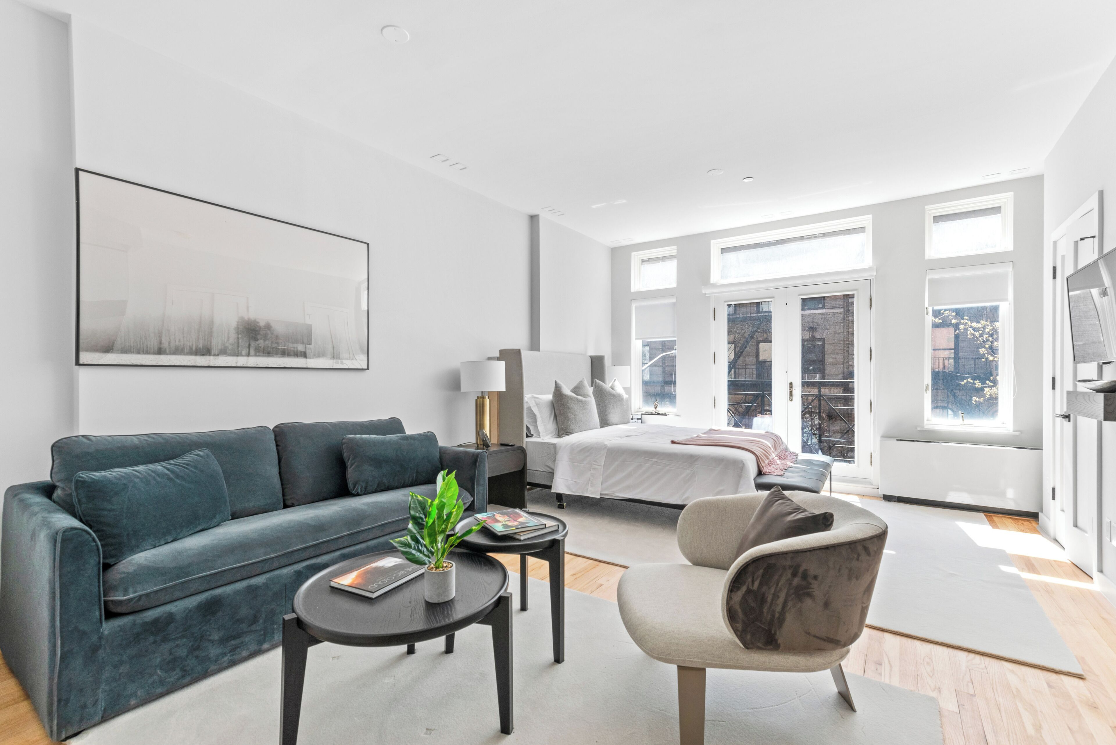 Ein modernes, helles Wohnzimmer mit einer Couch, einem Sessel, einem Couchtisch und einem Bett mit Blick auf die Stadt.
