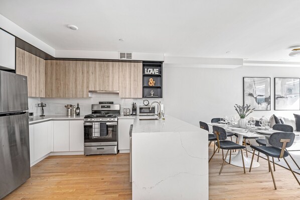 Una cocina moderna con armarios blancos, una isla central y un comedor con mesa y sillas blancas.