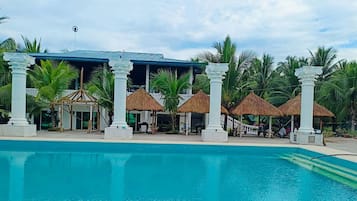 A pool area with a clear blue pool, white columns, and thatched-roof structures.